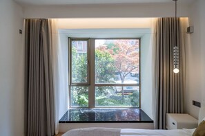 Una habitación de hotel con un ventanal grande, una cama, una mesita de noche y una lámpara.