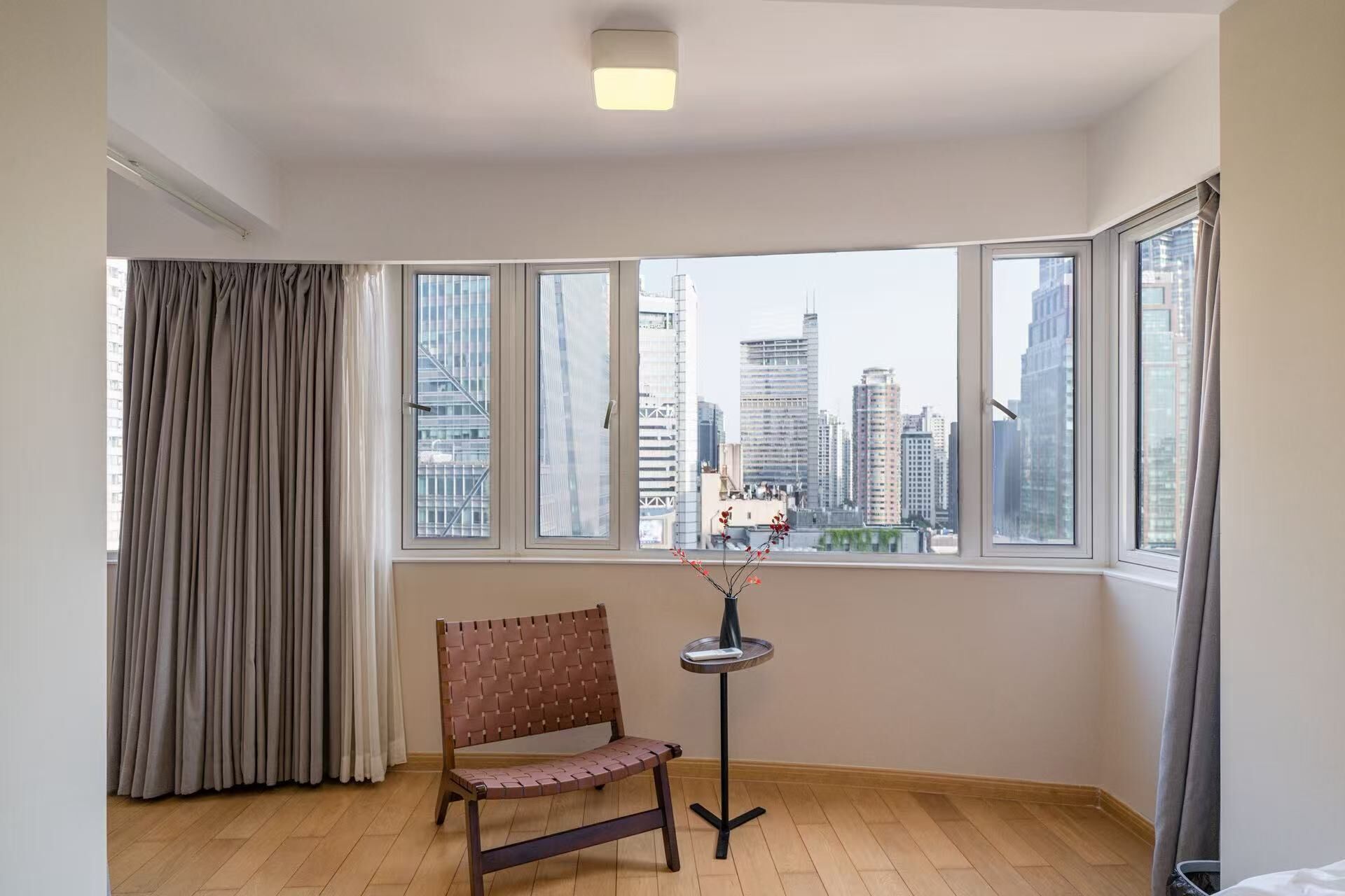 A corner room with a bench, a small table, and a view of a cityscape through large windows.