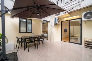 Un patio con mesa y sillas, una sombrilla grande y una puerta corrediza de vidrio que da a un dormitorio.