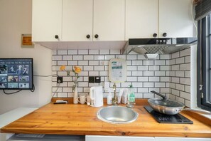 A kitchen with a wooden countertop, a sink, a stove, and a wall-mounted TV. - Book and Bed-Nanjing West Road (Shanghai)