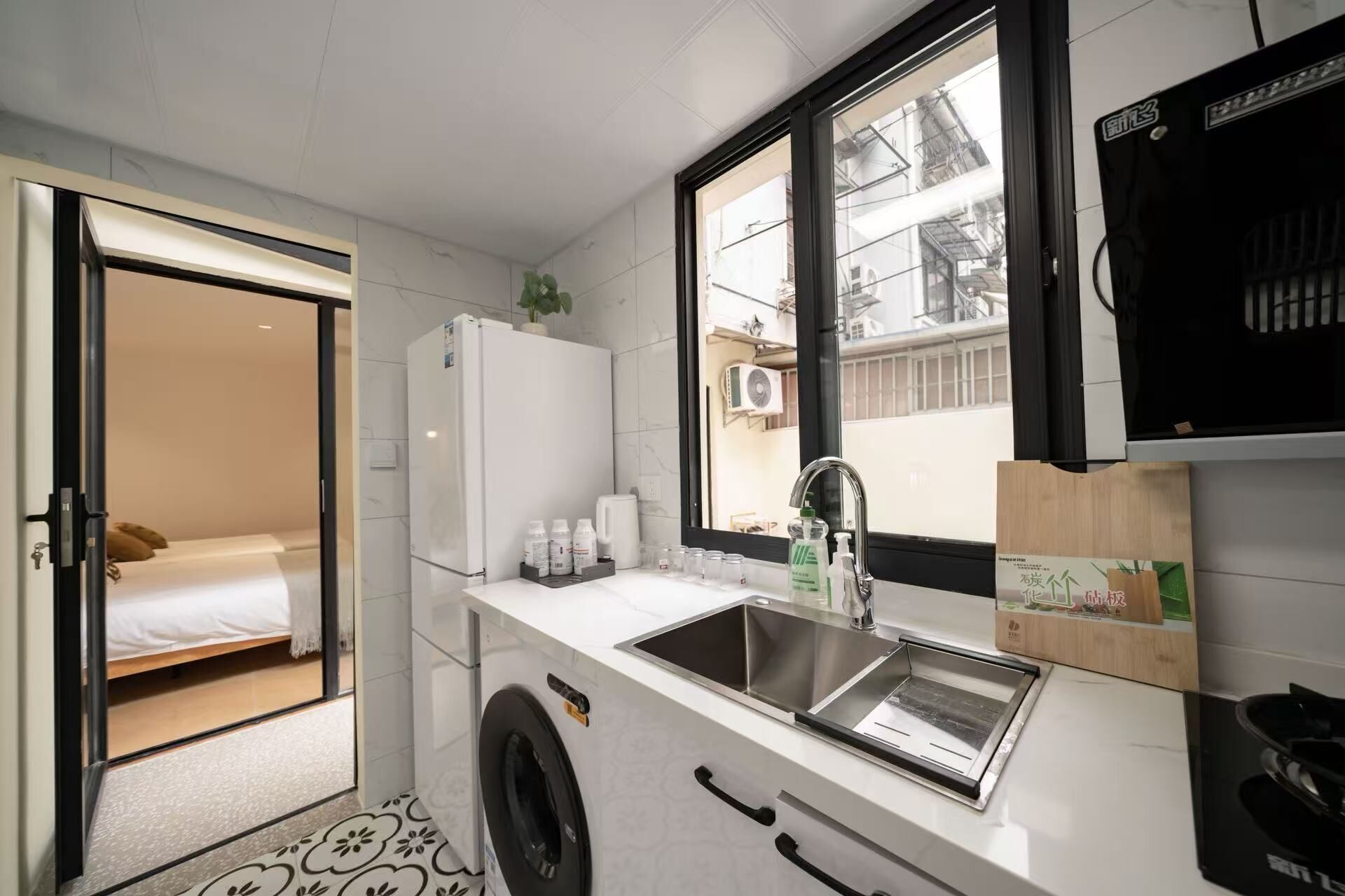 A compact kitchen with a washing machine, a sink, and a window with a view of buildings.