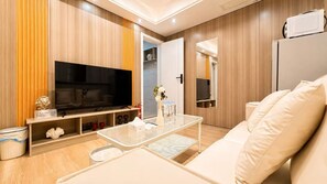 Una sala moderna con televisión de pantalla plana, una mesa de centro de vidrio, un sofá y un microondas en un mueble.