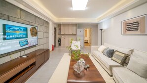 Un salon moderne avec un téléviseur à écran plat, une table basse en bois, un canapé et une cuisine en arrière-plan.