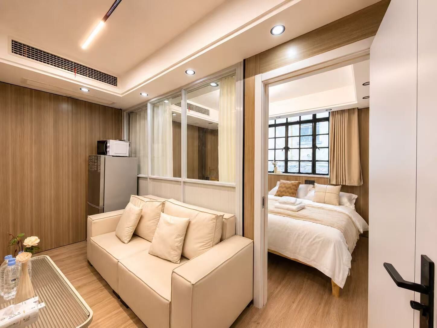 A hotel room with a sofa, a bed, a TV, and a window with curtains.