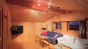 Ein Interieur einer Holzhütte mit einer Couch, einem Couchtisch und einem an der Wand befestigten Fernseher.