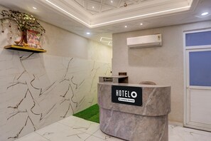 A reception desk with a 'HOTEL' sign, a reception area with a marble wall, a reception desk with a green carpet, and an air conditioning unit on the wall.