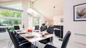 Uma sala de jantar moderna com mesa de madeira posta para quatro, cadeiras pretas e iluminação pendente.