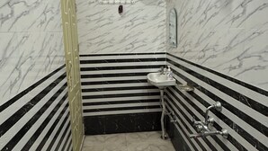 A bathroom with a white marble floor, a black and white striped wall, a white sink, and a white heater mounted on the wall. - Shri Ganapati Hotel BY S4S (Ukhimath)