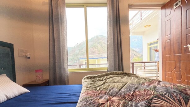A hotel room with a bed, a window with curtains, a view of the outside, and a door with a number. - Shri Ganapati Hotel BY S4S (Ukhimath)