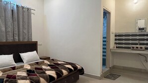 A bedroom with a bed, a ceiling fan, a bathroom with a striped sink, and a door leading to another room. - Shri Ganapati Hotel BY S4S (Ukhimath)