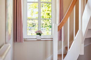 Un escalier avec une rampe blanche, une fenêtre donnant sur un paysage verdoyant et une plante en pot posée sur le rebord de la fenêtre.