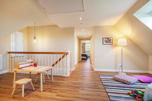 Ein geräumiger Raum mit Holzboden, einer Treppe, einem Tisch mit roher Matte, einer Lampe und einem farbenfrohen Teppich.