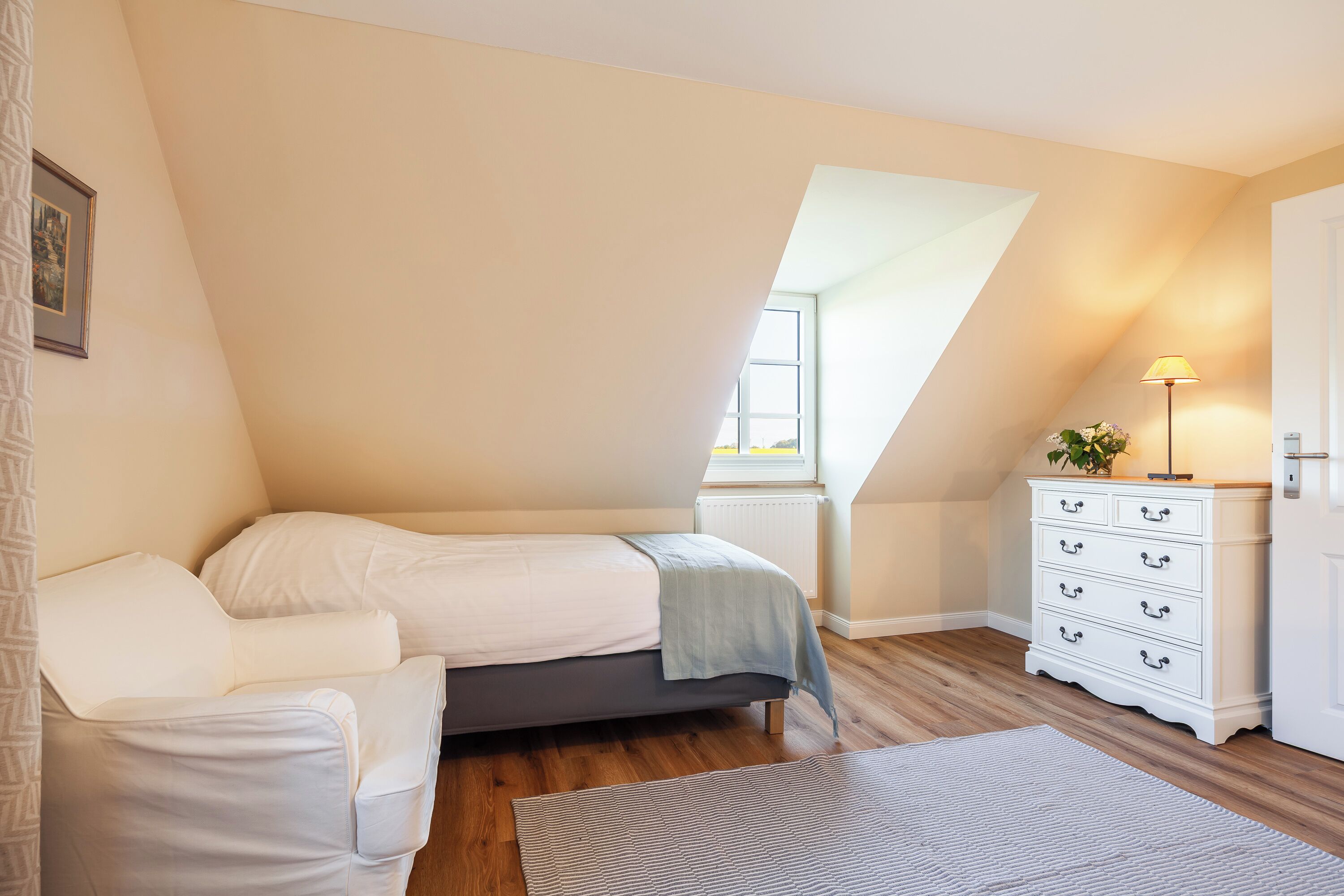 Ein Schlafzimmer mit einem Schlafpodest, einer weißen Kommode, einer Lampe und einem Fenster.