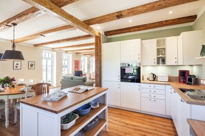 A modern kitchen with white cabinets, wooden beams, and a central island with a sink. - Vacation home Kreuzkate near Grömitz - Baltic Sea & fireplace (Manhagen)