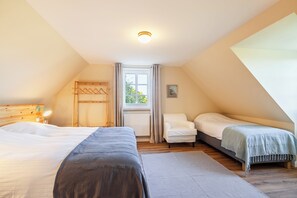 Une chambre avec un grand lit, un plus petit lit, une chaise et une fenêtre avec des rideaux.