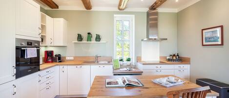 A modern kitchen with white cabinets, a wooden dining table, and a window.