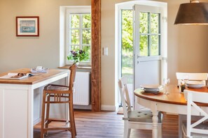 Ein Essbereich mit Holztisch und Stühlen, einem Fenster mit Blick auf Grünflächen und einem gerahmten Bild an der Wand.