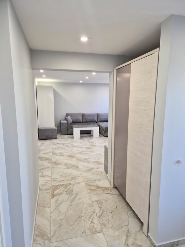 A hallway with a marble floor, a grey sofa set, a small white coffee table, and a wardrobe.