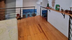 Une pièce spacieuse avec un plancher en bois, un lit, un balcon doté d’une balustrade et une étagère murale ornée d’objets décoratifs.