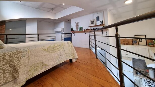 Une chambre avec un lit, un plancher en bois, un escalier et, au fond, un coin cuisine.