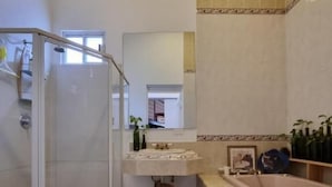 Une salle de bain avec une douche à parois de verre, un lavabo avec un miroir, une baignoire et un sol carrelé.