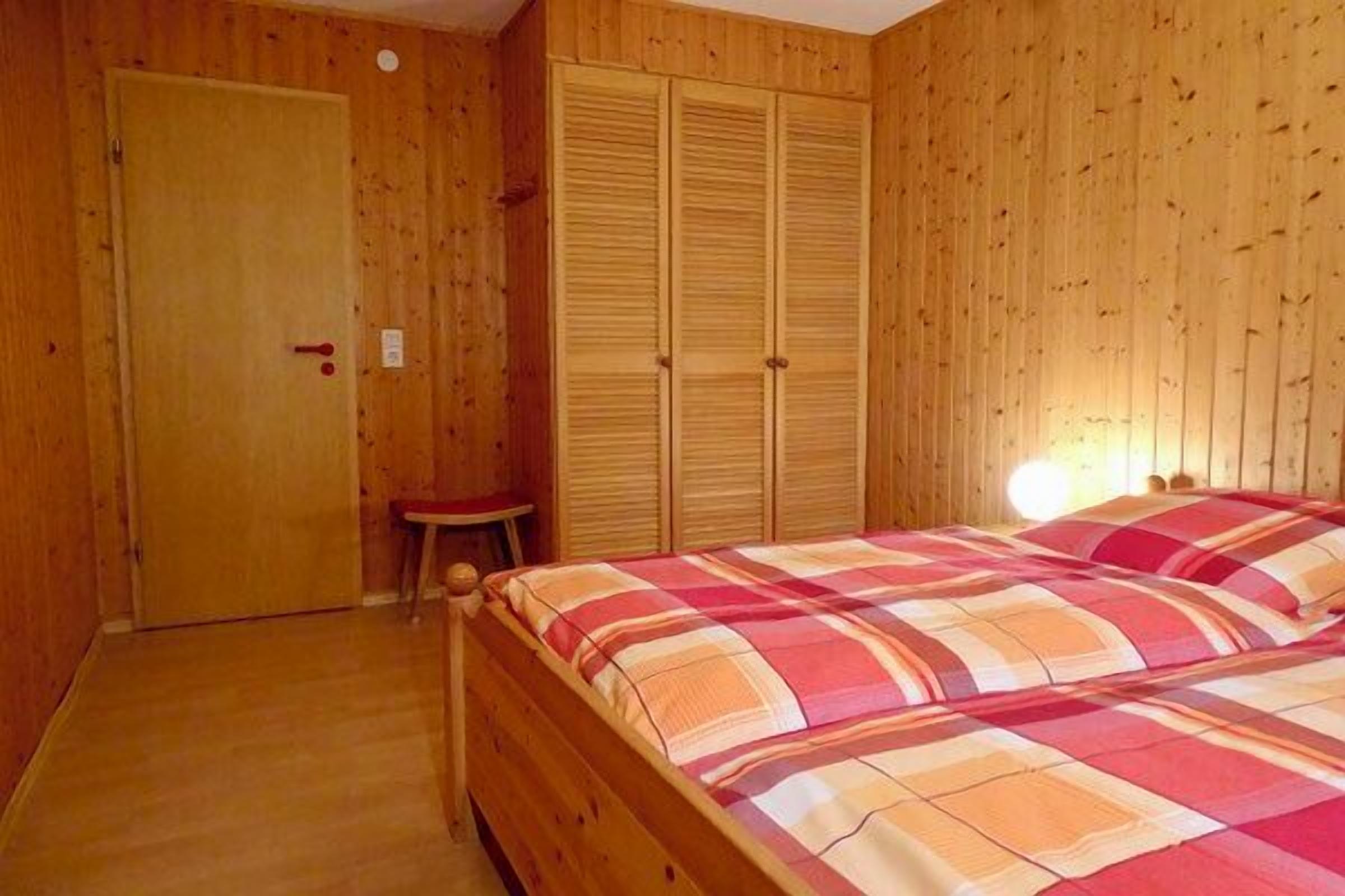 Een houten kamer met een bed, een deur en een klein krukje.