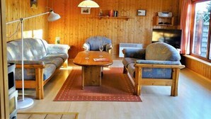 A cozy living room with wooden walls, a sofa, two armchairs, a coffee table, a floor lamp, and a television. - Ferienhof Birkblick "Tannengrün" (Gelting)