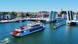 A river with a large boat docked at a pier, a bridge, and buildings in the background. - Ferienhof Birkblick "Tannengrün" (Gelting)