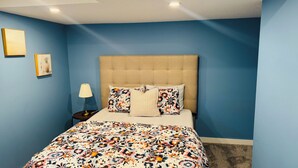 A bedroom with a bed, a nightstand, a lamp, and two framed pictures on the wall. - Entire Basement suite (Chestermere)