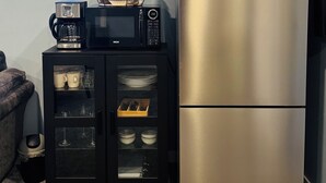 A kitchen with a stainless steel refrigerator, a black microwave, and a coffee maker on a black cabinet. - Entire Basement suite (Chestermere)