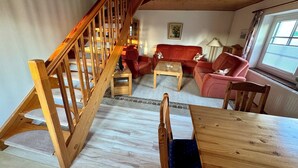 Uma escadaria de madeira leva a uma sala de estar com um sofá vermelho, uma mesa de centro e uma mesa de jantar de madeira.