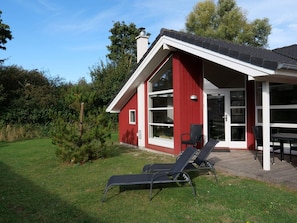 A red building with a covered patio, two lounge chairs, and a small window. - 4 Star Holiday Home in Grossenbrode (Grossenbrode)