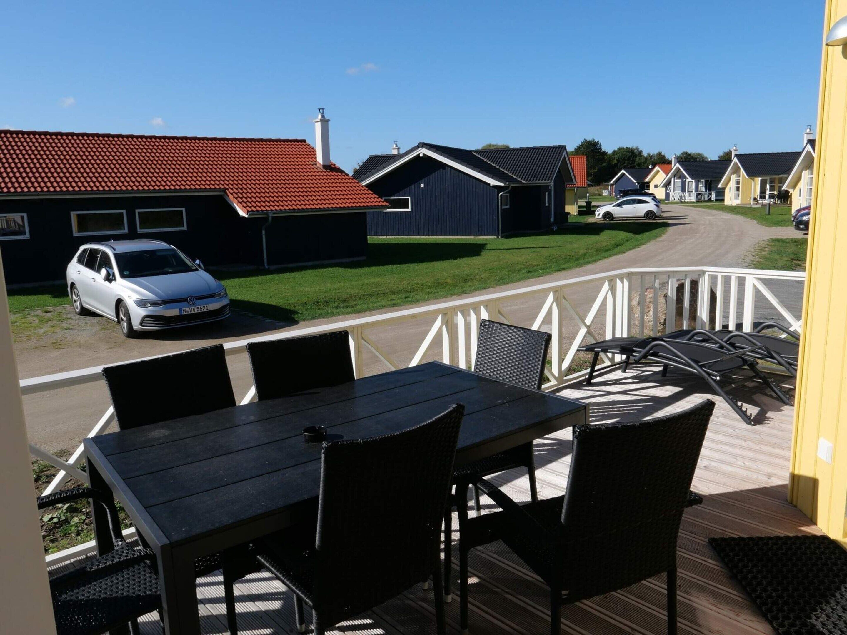 A deck with outdoor seating, a view of a street with houses, and a parked car.