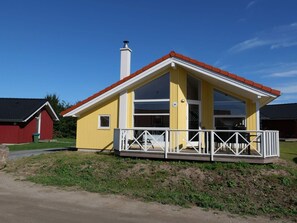 Ett gult hus med ett rött tak, en vit veranda och en skorsten.