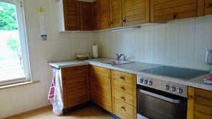 Una cocina con armarios de madera, un lavamanos, una estufa y una ventana con vistas al verdor.