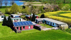 Zona residencial con una casa que cuenta con paneles solares, un cobertizo pequeño y un invernadero.