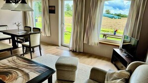 Una sala de estar con sofá, reposapiés, mesa de centro, televisor y un comedor con sillas y una mesa.