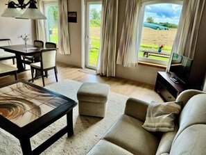 A living room with a sofa, ottoman, coffee table, TV, and a dining area with chairs and a table. - Ferienhof Birkblick "Green Meadow" (Gelting)