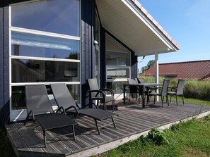 Ein modernes Haus mit einer überdachten Terrasse, großen Fenstern und Gartenmöbeln.