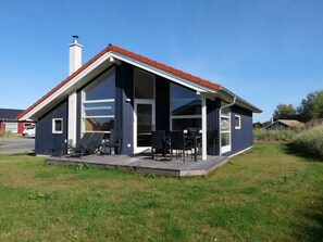 Ein modernes Haus mit großem Panoramafenster, einer überdachten Veranda und einem Schornstein.