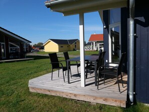 Eine überdachte Terrasse im Freien mit Tisch und Stühlen, eine Holzterrasse und Blick auf Nachbarhäuser.