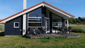 Ett modernt hus med en stor glasdörr, en skorsten och en terrass med utemöbler.