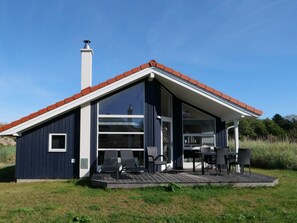 A modern house with a large glass door, a chimney, and a deck with outdoor furniture. - 4 Star Holiday Home in Grossenbrode (Grossenbrode)