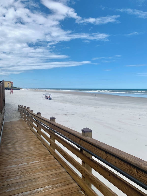 A wooden boardwalk leading to a beach with a clear sky. - Spectacular ocean view on no drive beach + heated rooftop saltwater pool (New Smyrna Beach)