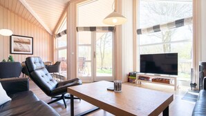 A modern living room with a wooden ceiling, large windows, a sofa, a table, and a television. - 4 Star Holiday Home in Grossenbrode (Grossenbrode)