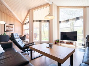 A modern living room with a wooden ceiling, large windows, a sofa, a table, and a television. - 4 Star Holiday Home in Grossenbrode (Grossenbrode)