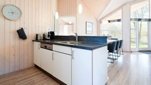 A modern kitchen with wooden walls, a central island, and a dining area with chairs. - 4 Star Holiday Home in Grossenbrode (Grossenbrode)