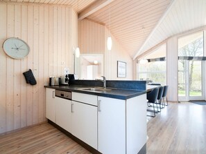A modern kitchen with wooden walls, a central island, and a dining area with chairs. - 4 Star Holiday Home in Grossenbrode (Grossenbrode)