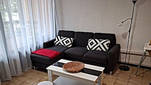 Una sala de estar con un sofá negro, dos otomanas negras, una mesa de centro blanca y una lámpara de pie.