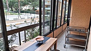Un interior moderno con una mesa y taburetes de madera, ventanas amplias que ofrecen vistas al exterior, y una estantería metálica a la derecha.